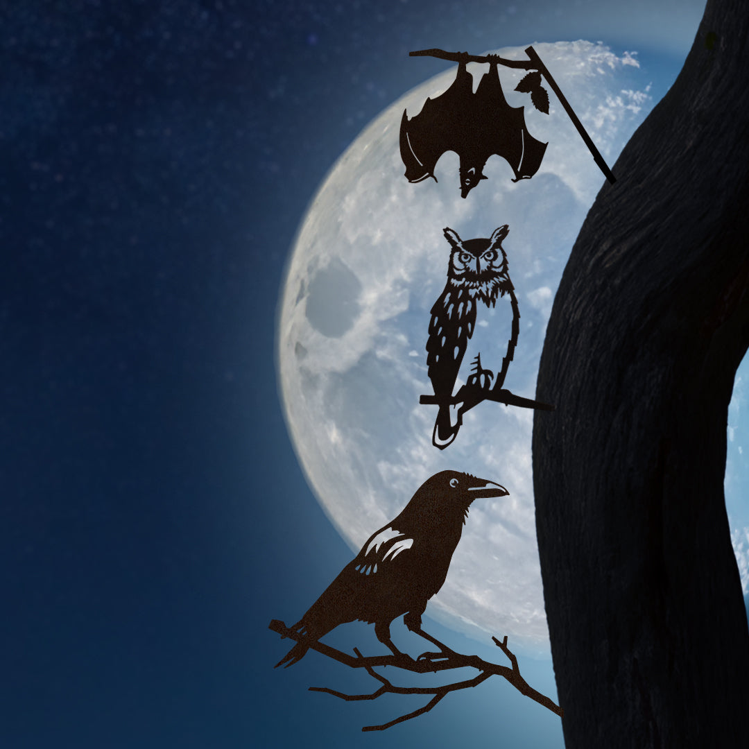 Corten steel crow, owl, and bat silhouettes perch on a tree branch under a full moon. Spooky garden art gift.