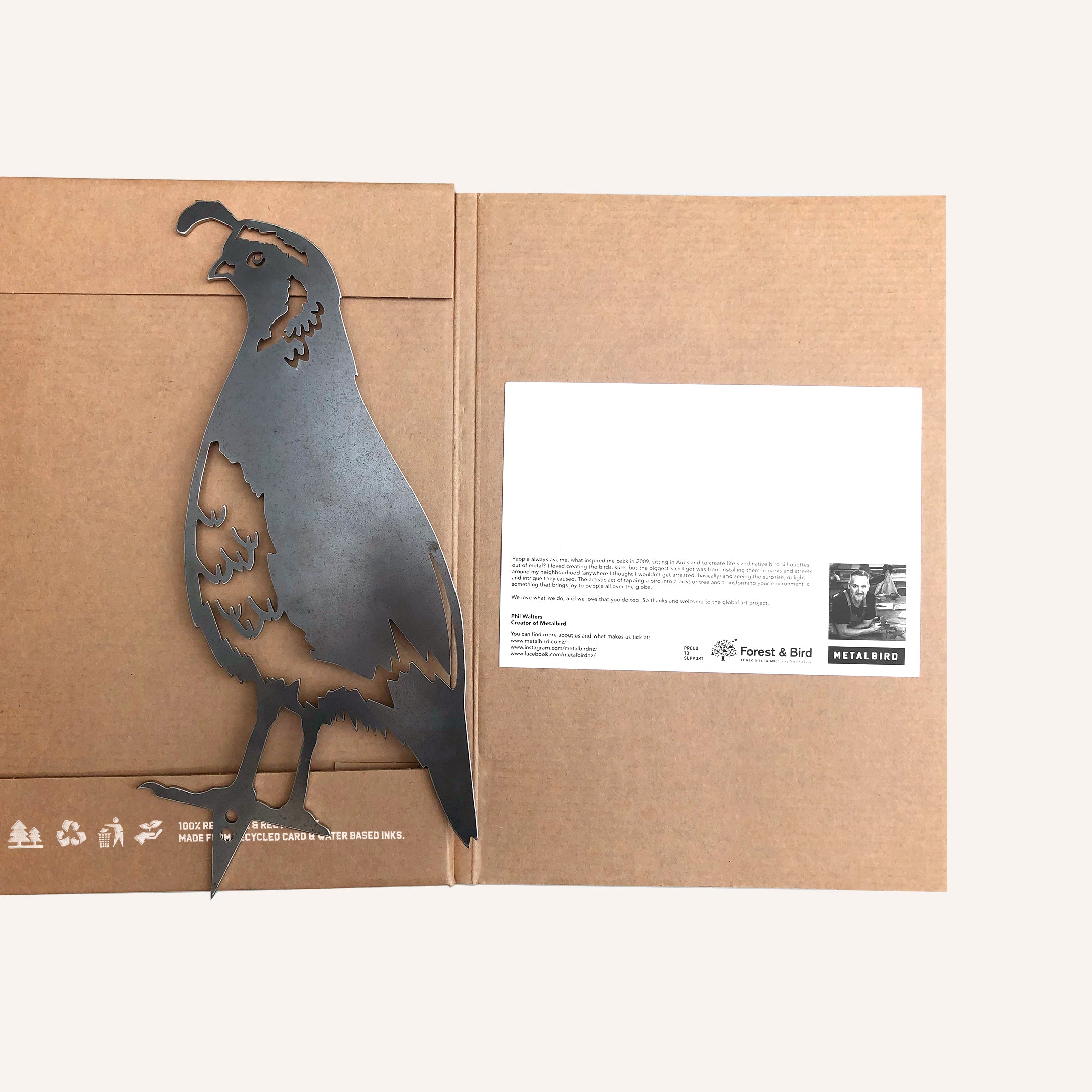 The California Quail is a metal silhouette crafted from corten steel, attached inside a brown cardboard folder with a white card on the right. The folder is open on a light surface, creating an elegant gift presentation.