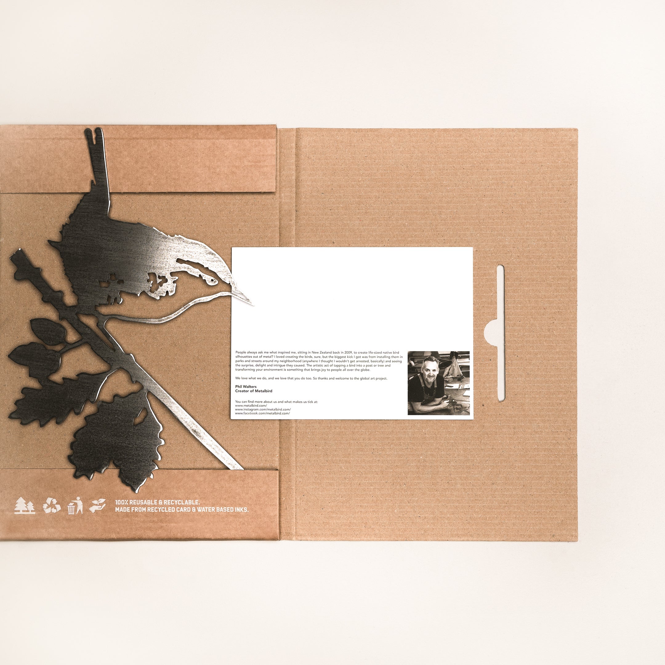 A brown cardboard gift box called "Wren" features a metal bird and leaf silhouette on the left and a white card with text and a small black-and-white portrait on the right, set against a plain, light background.