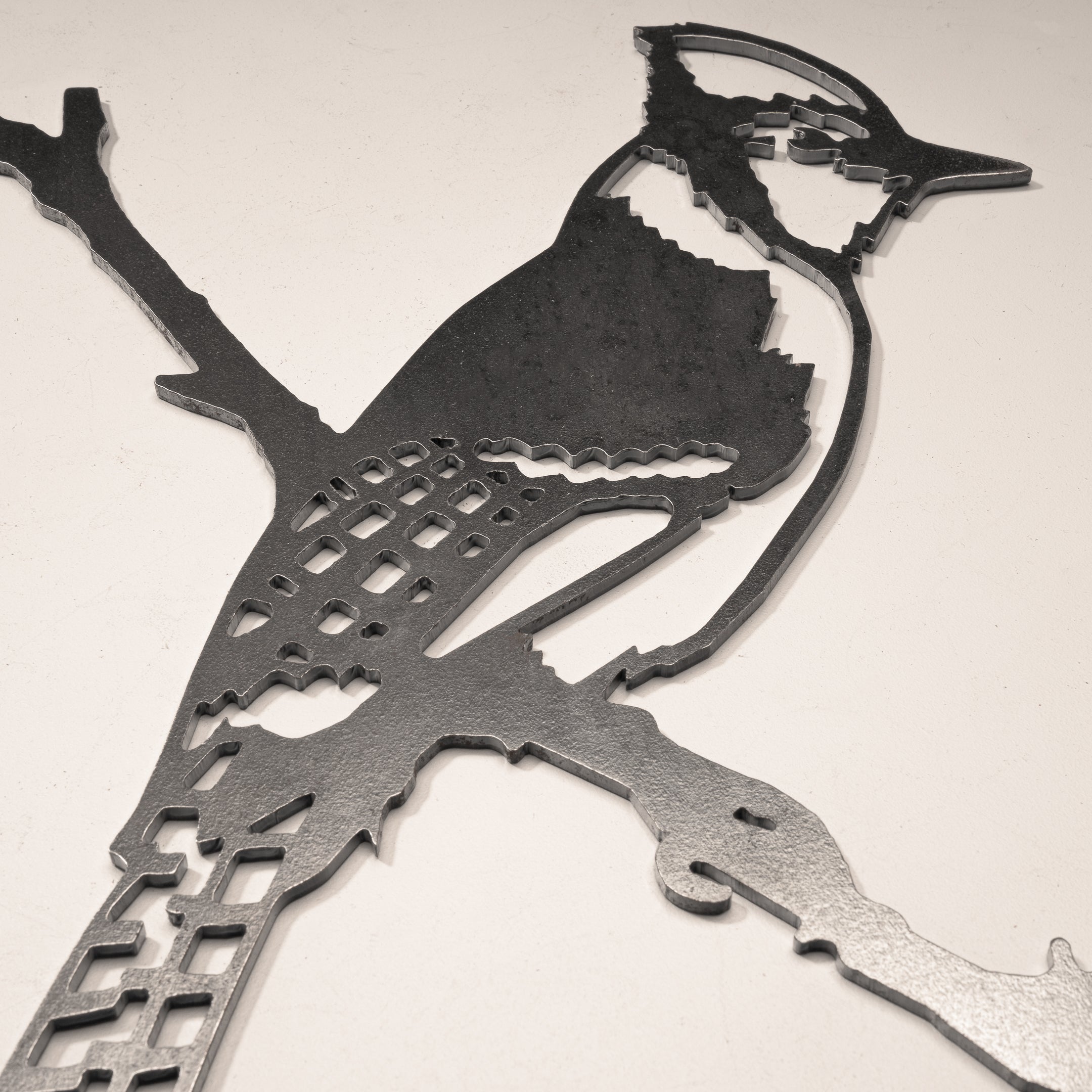 Blue Jay is a premium metal art piece featuring a stylized bird perched on a branch with geometric cutout wings and body, displayed on a light surface—an ideal gift for any art lover.