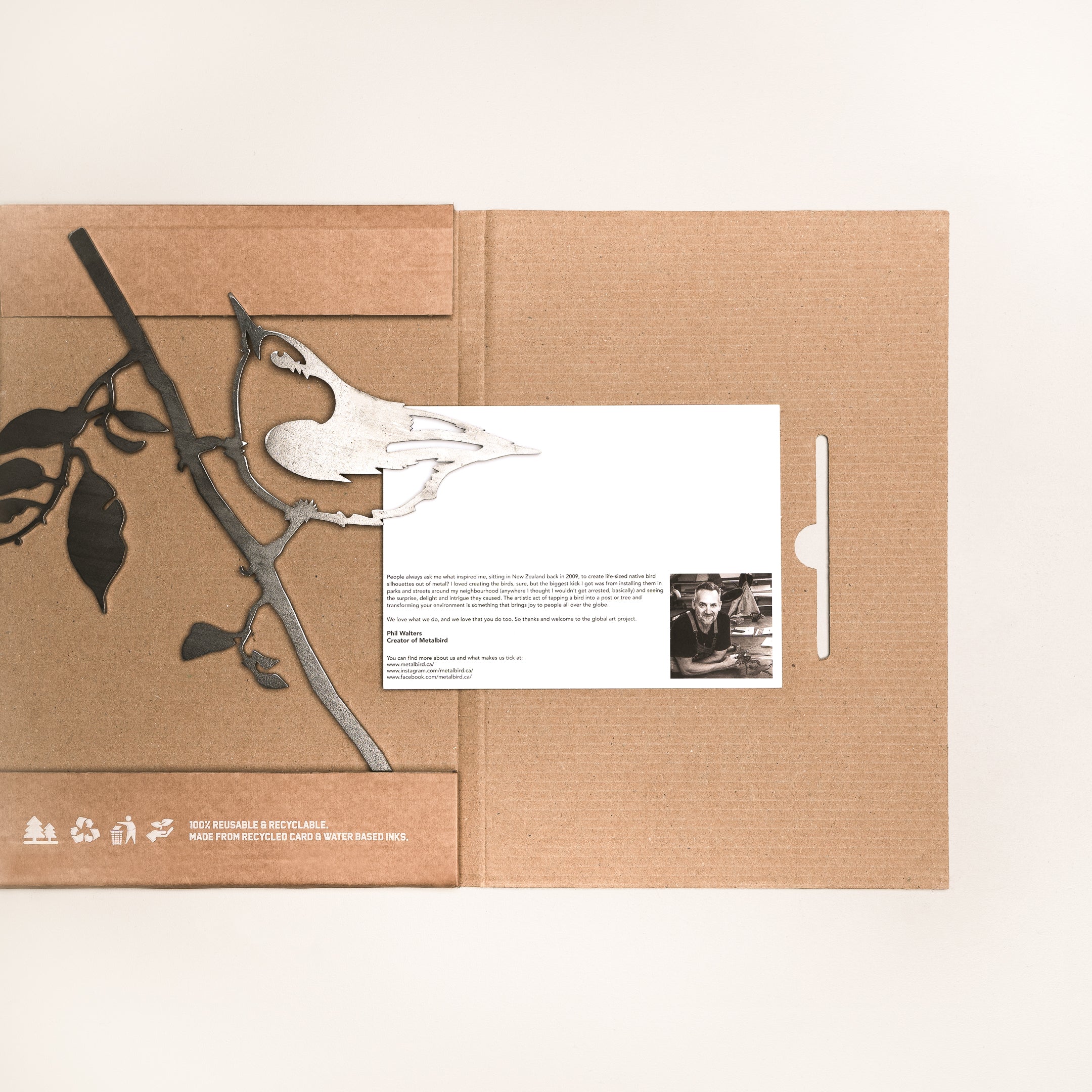 A cardboard package with a branch and bird silhouette design holds the "Nuthatch" card, featuring text and a small black-and-white photo. The partially opened package reveals the card—ideal for fans of unique yard art.