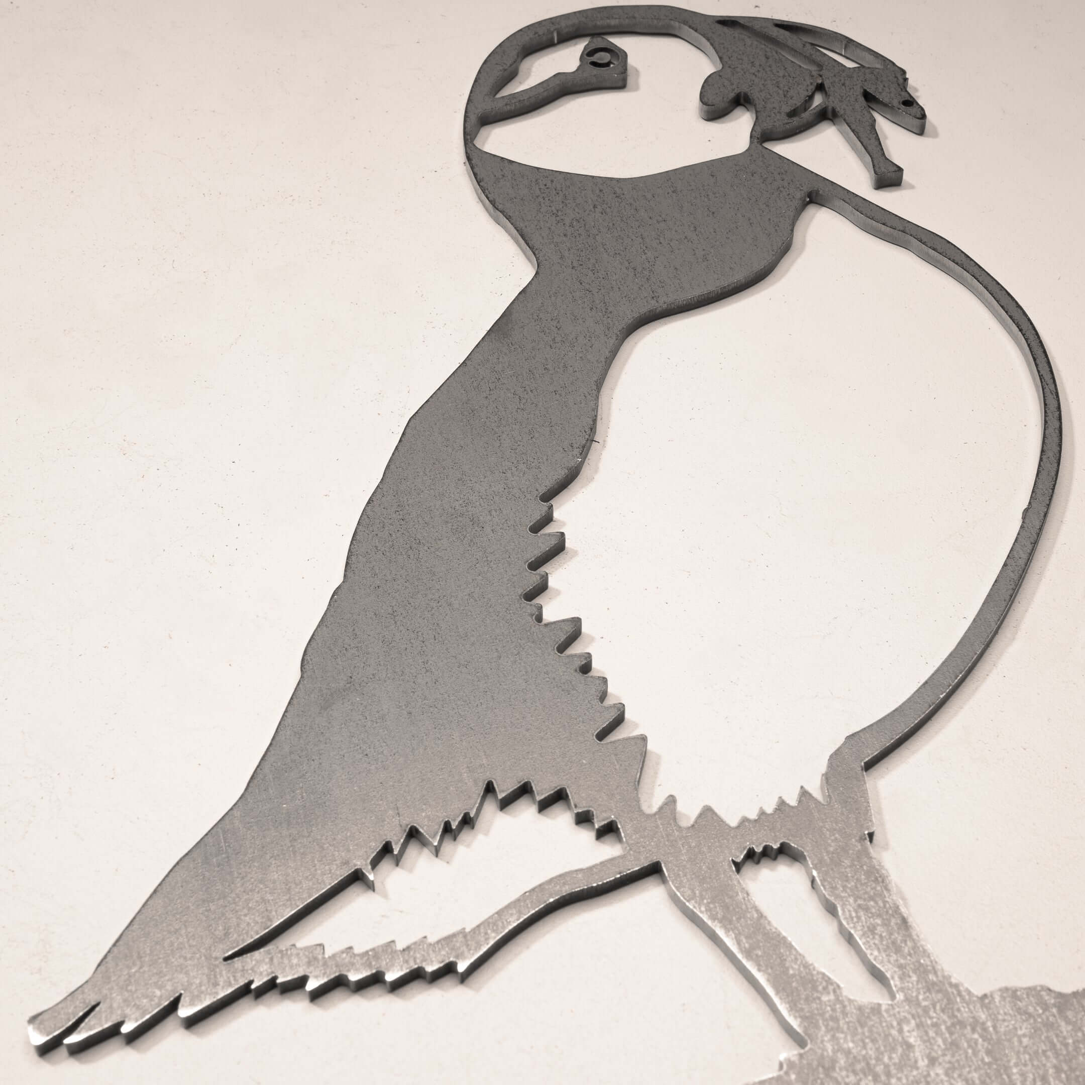 The Puffin is a striking metal wall art sculpture with a minimalist silhouette cutout, perfect for bird and art lovers as a stylish gift or decor accent on any light-colored wall.