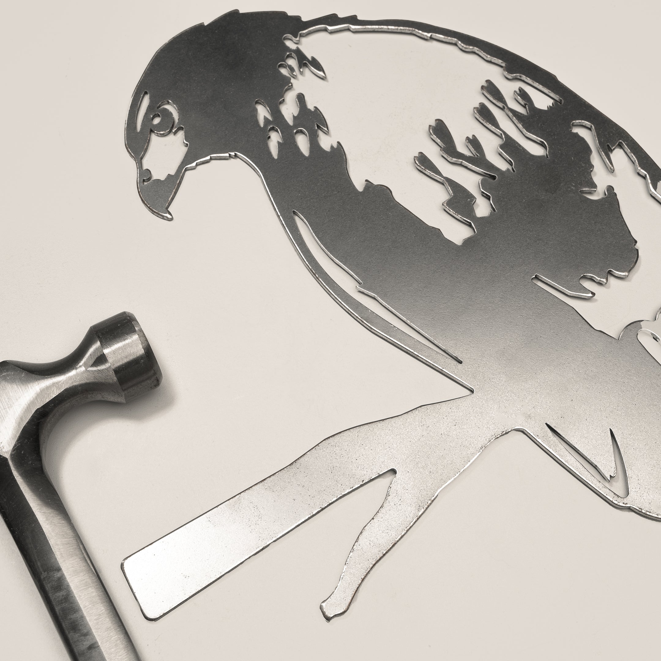 A premium metal Red-Tailed Hawk silhouette perches on a white surface beside a hammer, suggesting an elegant crafting project or unique gift idea.