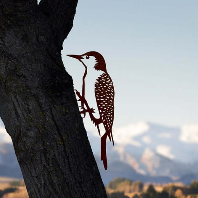 Woodpecker silhouette of Corten steel perched on branch against mountain scenery garden art.