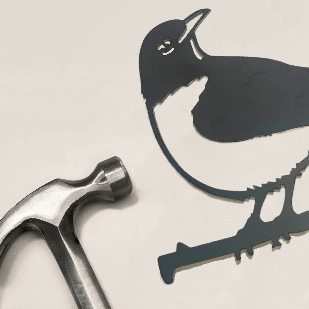 A metal hammer lies next to the American Robin, a black-and-white metal bird silhouette ideal as unique yard art or a thoughtful gift, on a white surface.