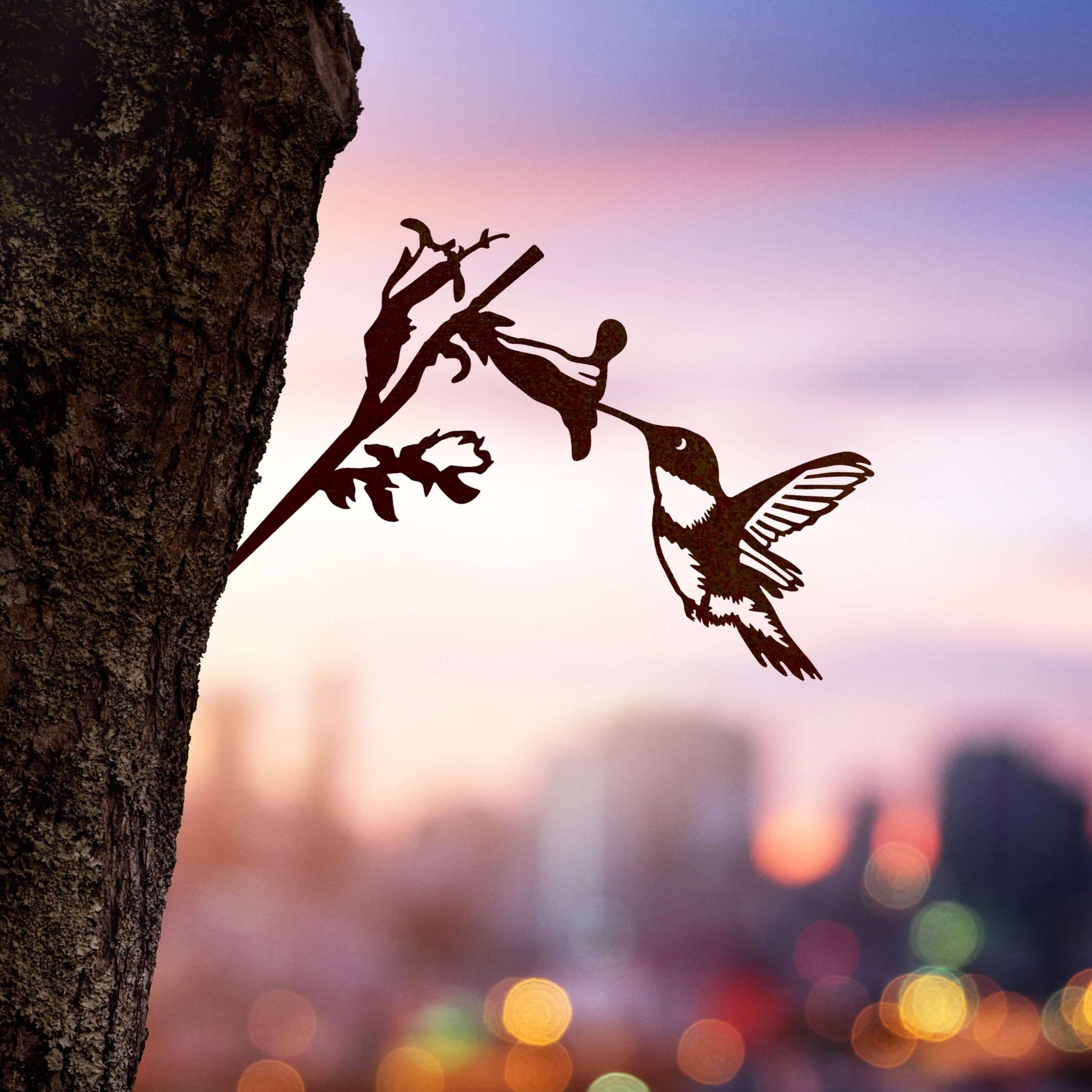 Corten steel Hummingbird sculpture tapping into a tree at sunset. Striking outdoor bird art. Perfect gift for bird lovers.