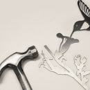 A metal hammer rests beside the Hummingbird Mom & Mini Set—intricately cut Corten steel hummingbird, flower, and branch accents—making a unique garden gift, displayed on a light surface.