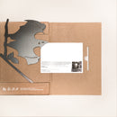 The Bat product is a cardboard folder holding a large black bat-shaped cutout for creative yard art, plus a white sheet with printed text and a small photo. The folder has white text and icons in the bottom left corner.
