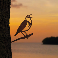 Meadowlark: A Corten steel sculpture inspired by the state bird’s silhouette perched on a branch at sunset, with tranquil water and an island in the background.