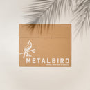 A brown cardboard envelope features a white illustration of the Osprey and the text METALBIRD PROUDLY MADE HERE IN AMERICA. A palm leaf shadow highlights support for bird conservation.