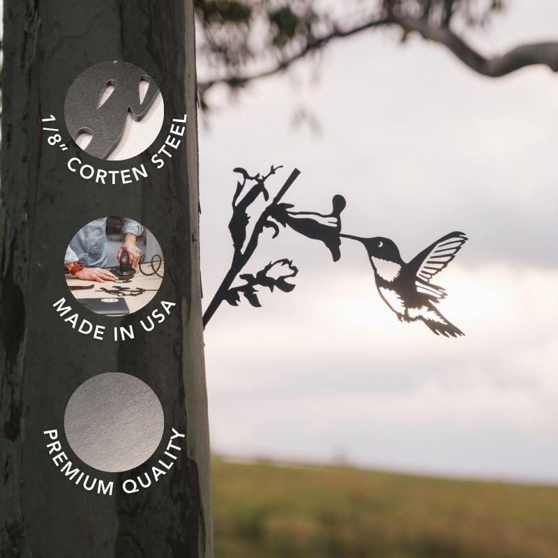A metal silhouette named "Hummingbird," crafted from 1/8 inch Corten steel, features a Ruby-Throated Hummingbird and flower attached to a tree, creating charming garden decor. Overlays read: "1/8 Corten Steel," "Made in USA," and "Premium Quality." A blurred landscape and sky appear in the background.