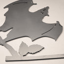The Bat is a corten steel silhouette featuring a bat with outstretched wings perched above a leaf. Detailed wings and facial features stand out against a light background, making it ideal as unique yard art.