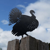 The Turkey features a premium metal silhouette mounted on a weathered wooden post, set against a partly cloudy blue sky.
