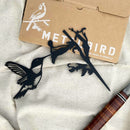 Black powder?coated Hummingbird silhouette flat?lay dark finish contrasted with natural background.