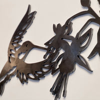The "Ruby-Throated Hummingbird" is a laser-cut Corten steel artwork showcasing a stylized hummingbird hovering by a flower, with intricate cut-out details on a light background.