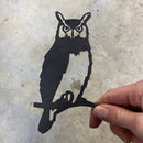 A hand holds the Mini Owl—a premium black metal cutout shaped like an owl on a branch, featuring detailed eyes and feather outlines—set against a plain, light background; a perfect gift for nature lovers.