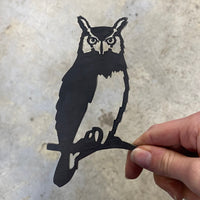 A hand holds the Mini Owl—a premium black metal cutout shaped like an owl on a branch, featuring detailed eyes and feather outlines—set against a plain, light background; a perfect gift for nature lovers.