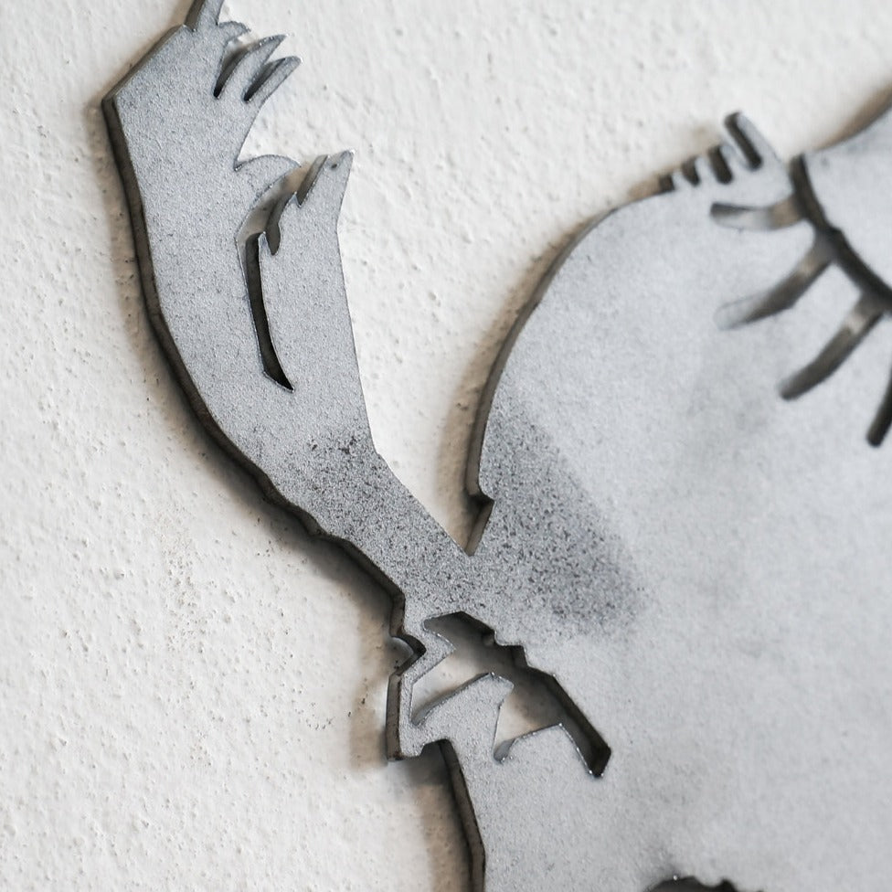Close-up of Metalbird Seconds - Chickadee & Chicks, a corten steel sculpture on a textured white wall, featuring jagged edges and abstract cutouts—perfect as striking modern yard art or an eye-catching silhouette.
