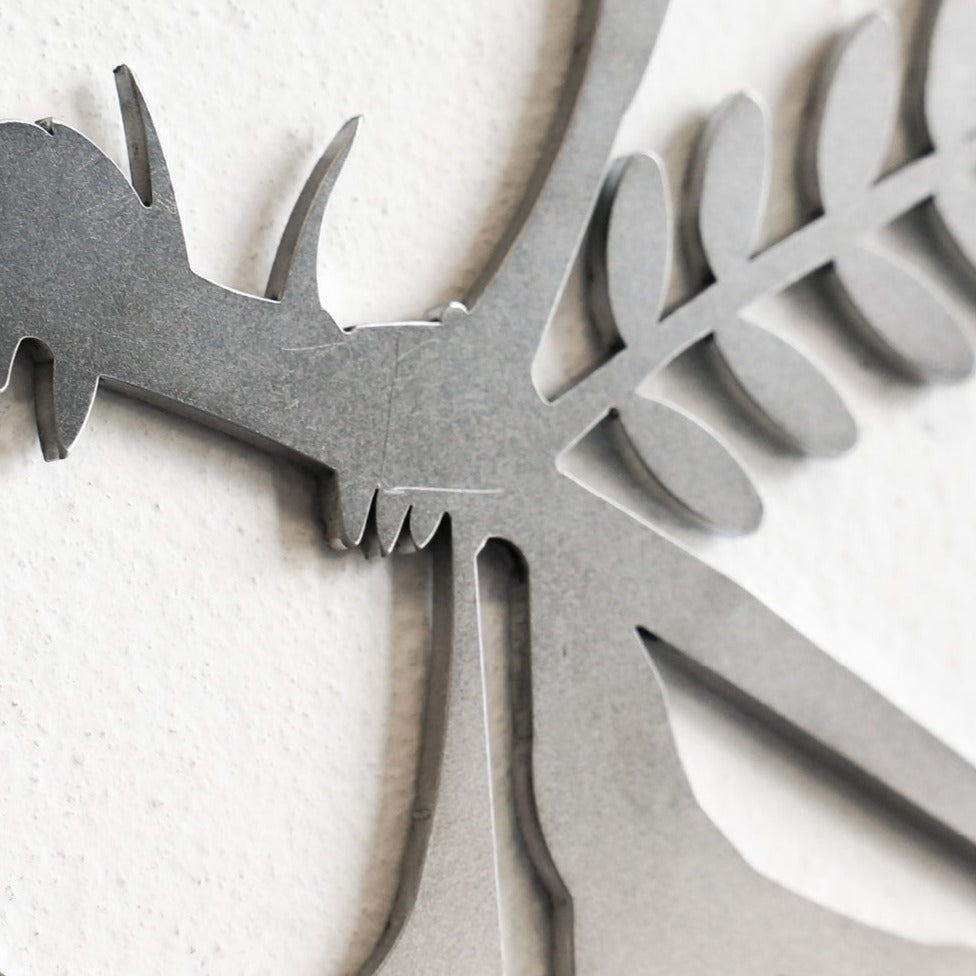 Close-up of Metalbird Seconds - Black Stilt, a minimalist metal wall art piece depicting a stylized insect with antennae and leaf-like wings, possibly with slight cosmetic imperfections, displayed on a textured white wall.
