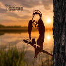 A metal silhouette of an Osprey perches on a branch attached to a tree trunk, with a lake and sunset in the background. The American Bird Conservancy logo, promoting bird conservation, is displayed in the upper left corner.