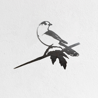 Metalbird Seconds - Canada Jay: A minimalist black metal silhouette of a Canada Jay on a branch with two leaves. Mounted on a white textured wall. Part of our seconds collection and may have minor cosmetic flaws.