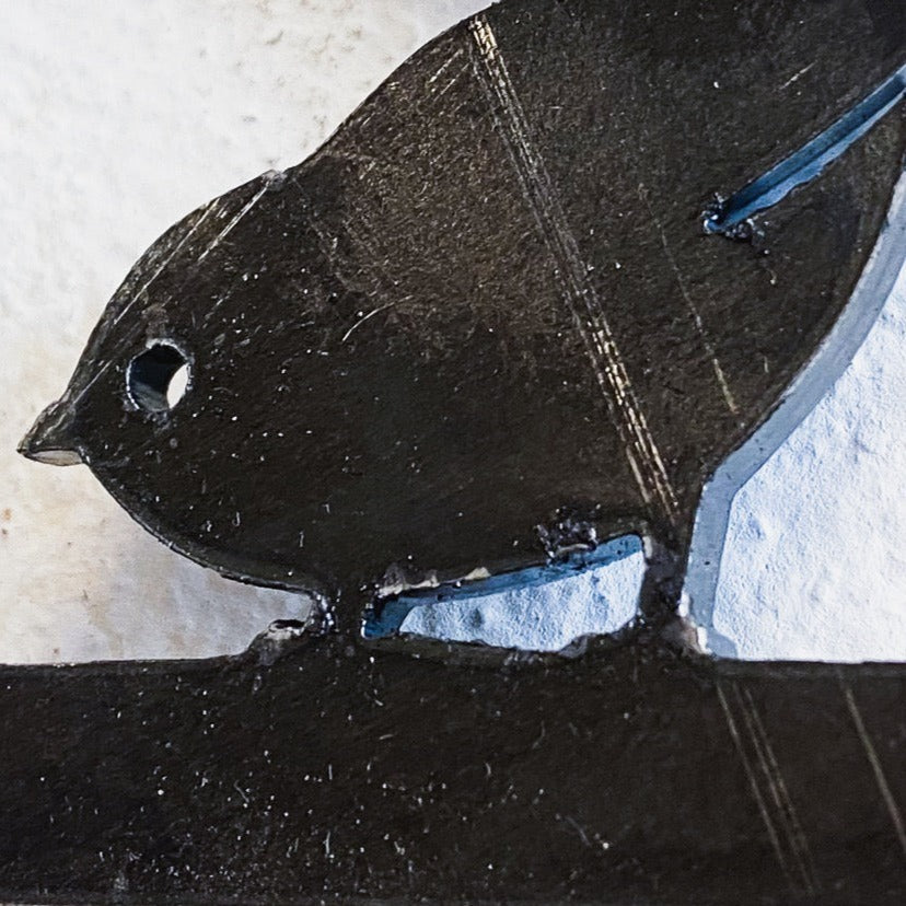 A close-up of the Metalbird Seconds - Pileated Woodpecker, a premium black metal bird silhouette, displayed against a light, textured background.