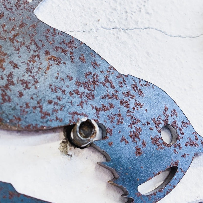 A close-up of the Metalbird Seconds - Chickadee, crafted from premium corten steel with visible rust spots, is mounted on a white cracked wall and secured with a screw at the attachment point.