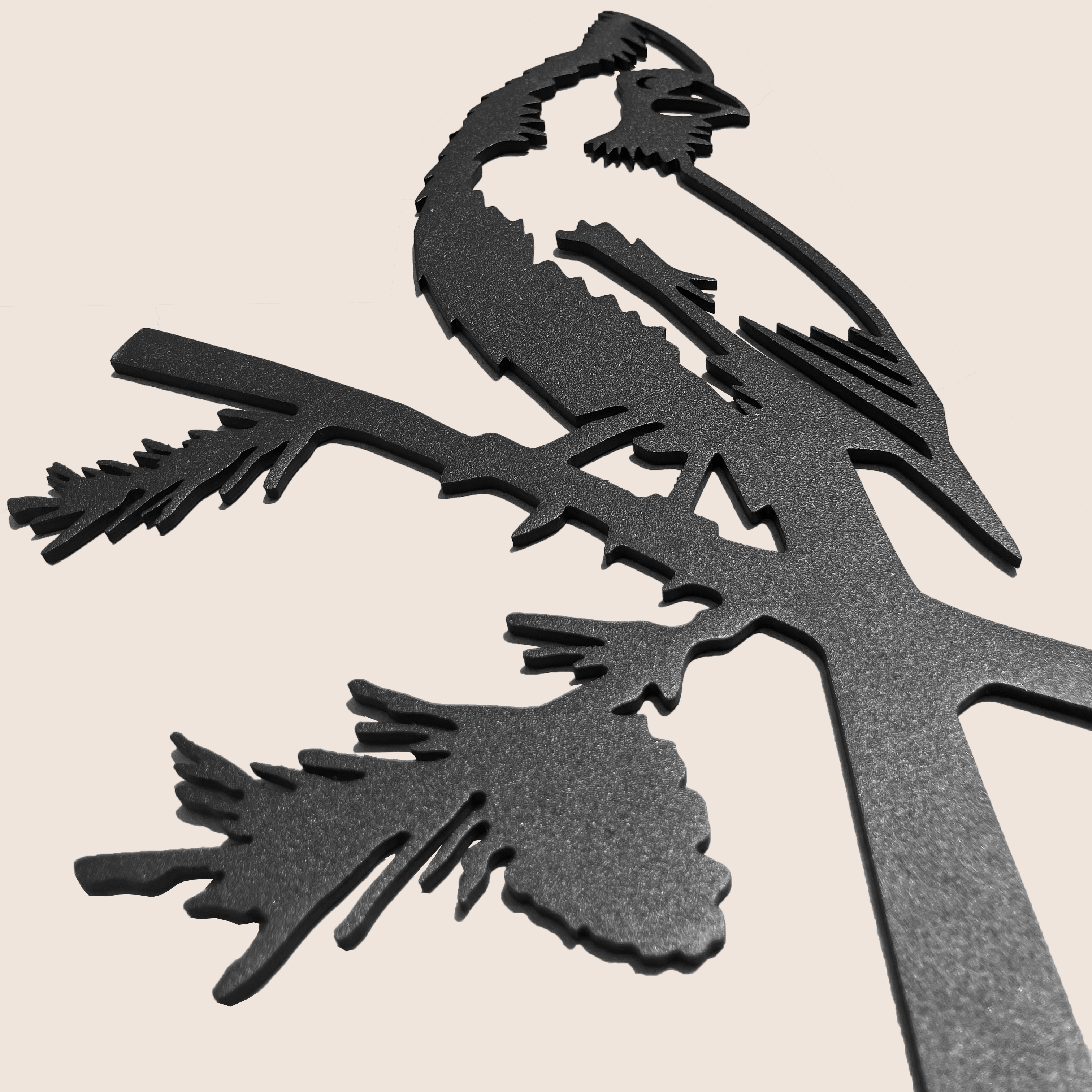 Cardinal Black features a powder-coated black metal silhouette of a cardinal perched on a branch, with intricate pine needle and pinecone cutouts, displayed against a light beige background.