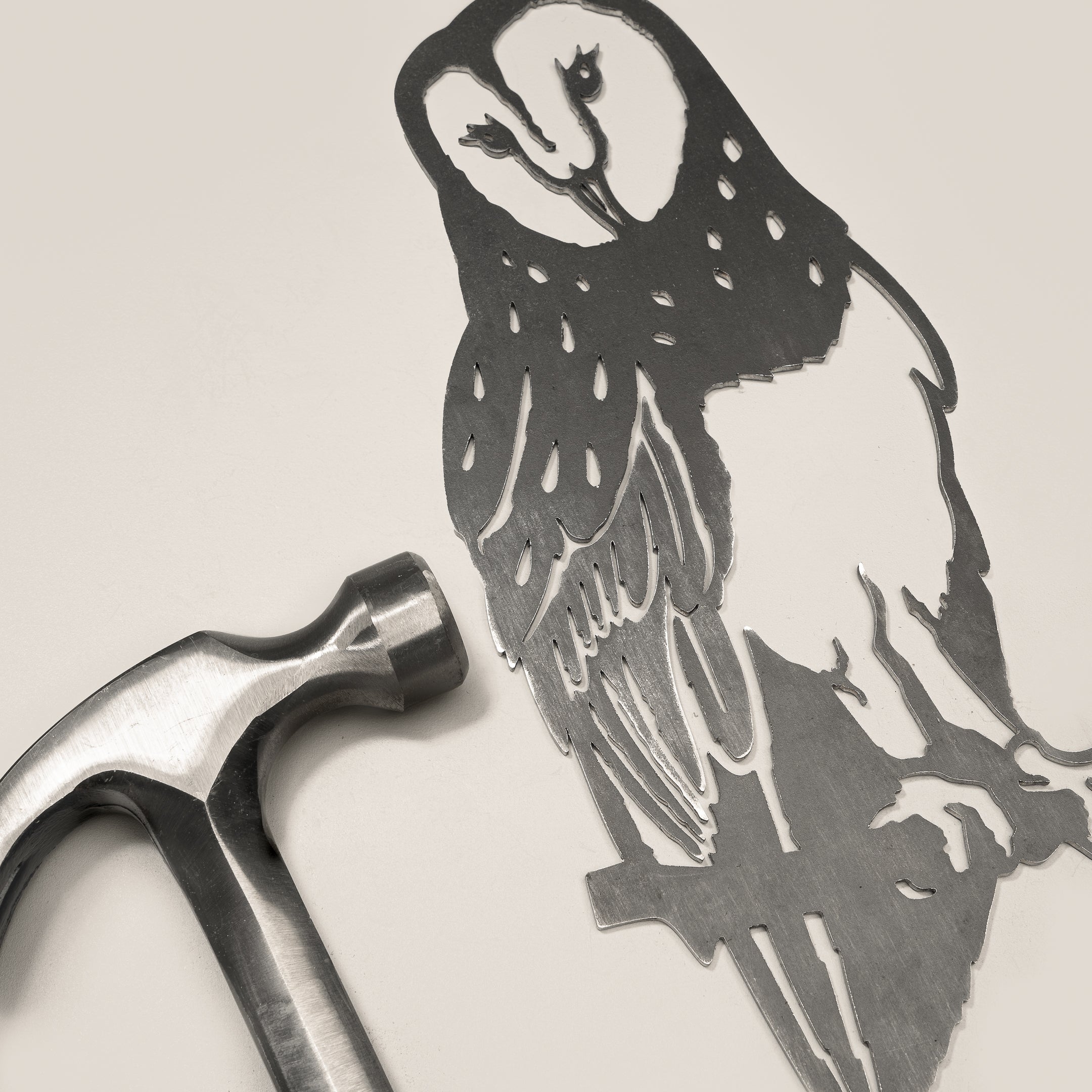 The Barn Owl, a detailed Corten steel cutout of an owl perched on a branch, is placed on a light surface beside a silver hammer.