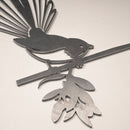 The Fantail (The New Zealand Piwakawaka) is metal wall art depicting a stylized fantail bird with its fanned tail on a leafy branch, crafted from Corten steel—ideal as an eye-catching garden ornament for any light background.