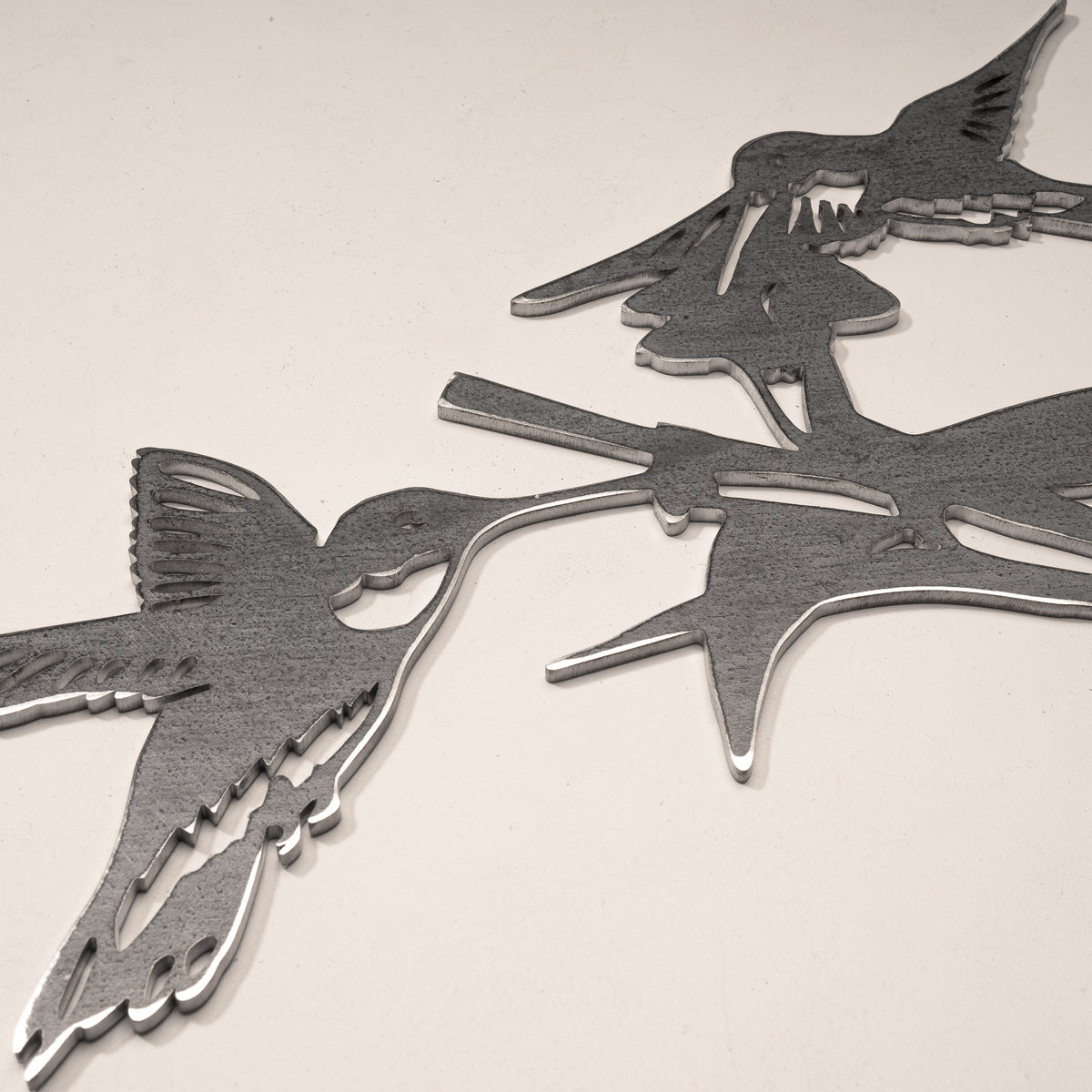 Close-up of the two hummingbird and leaf cutouts in gray steel.