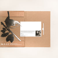 A brown cardboard gift box called "Wren" features a metal bird and leaf silhouette on the left and a white card with text and a small black-and-white portrait on the right, set against a plain, light background.