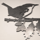 A corten steel silhouette cutout named "Wren" features a bird perched on a leafy branch, displayed on a light surface with a soft, sepia tone—ideal as a distinctive gift or delightful decor accent.