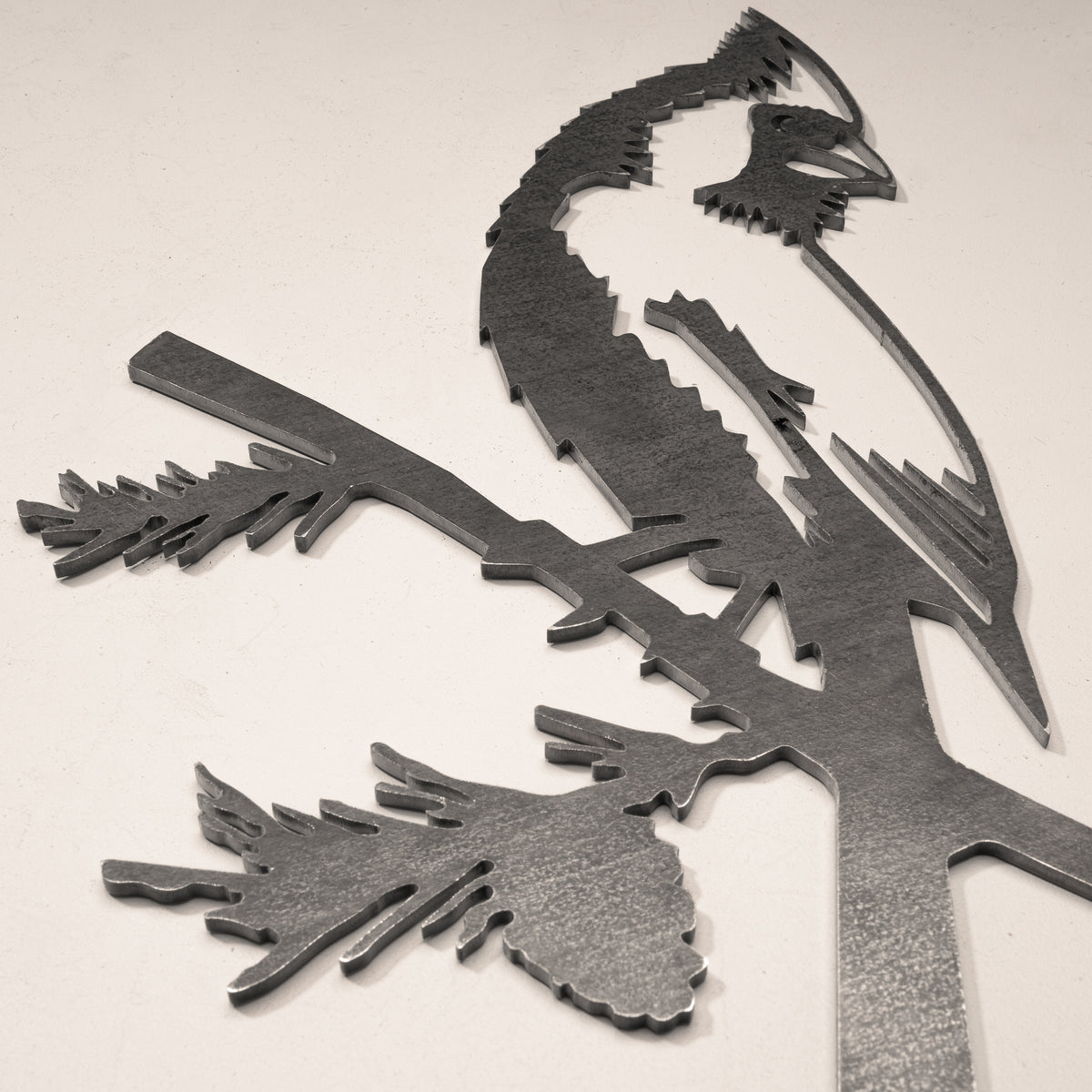 Close-up of the Cardinal silhouette and pine-branch cutout in gray steel.