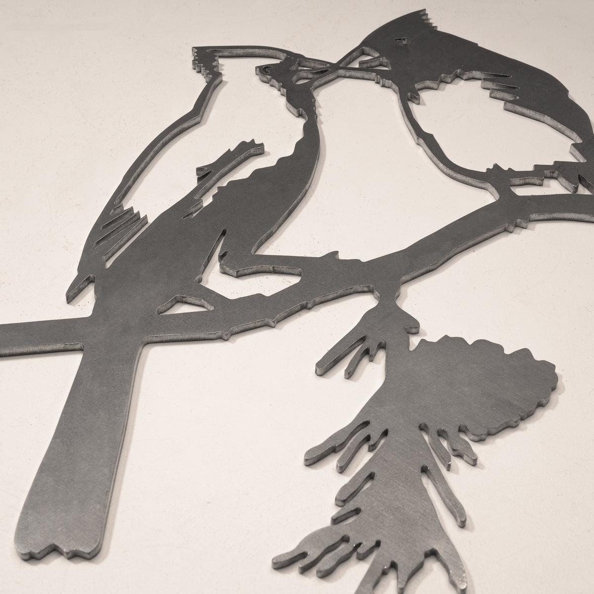 Close-up of the two cardinal faces and shared pine branch in steel.