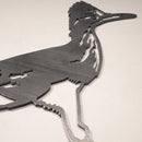 The Road Runner is a geometric, stylized metal wall art sculpture crafted from Corten steel. Highlighting the bird’s crest, beak, and long legs, this outdoor decor features angular lines and looks striking on a light-colored wall.