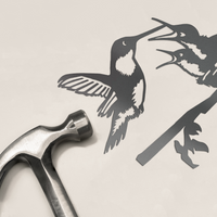 A silver hammer lies beside the Hummingbird & Chicks metalbird silhouette—two corten steel birds on a branch, facing each other—a charming decor piece and perfect Mother’s Day gift.