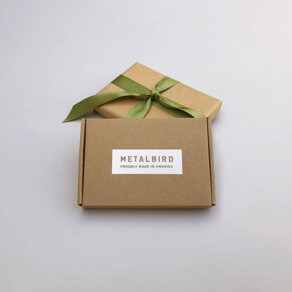Two brown cardboard gift boxes—one with a green ribbon, the other labeled METALBIRD PROUDLY MADE IN AMERICA—showcase the Baby Bird Bundle - Hummingbird Trio, crafted from durable Corten steel, on a simple light background.