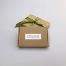 Two brown cardboard gift boxes—one with a green ribbon, the other labeled METALBIRD PROUDLY MADE IN AMERICA—showcase the Baby Bird Bundle - Hummingbird Trio, crafted from durable Corten steel, on a simple light background.