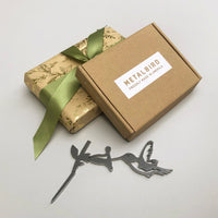 A wrapped gift with a green ribbon, a brown METALBIRD box labeled Proudly Made in America, and a Corten steel silhouette from the Baby Bird Bundle - Hummingbird Trio with mini hummingbirds and a branch on a light background.