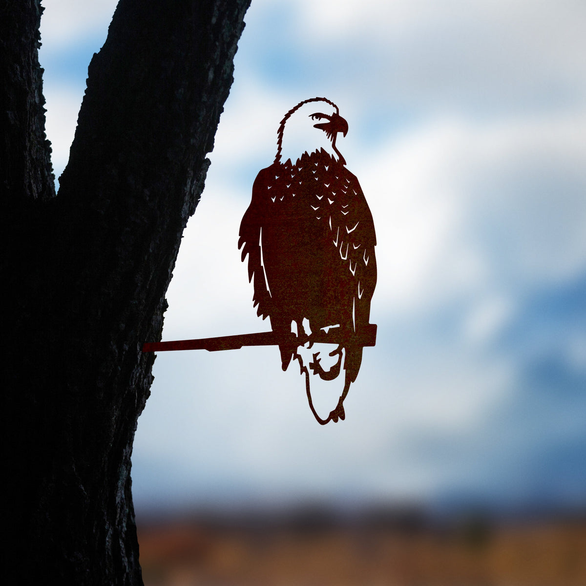 Bald Eagle steel silhouette mounted beside a tree trunk at dusk.