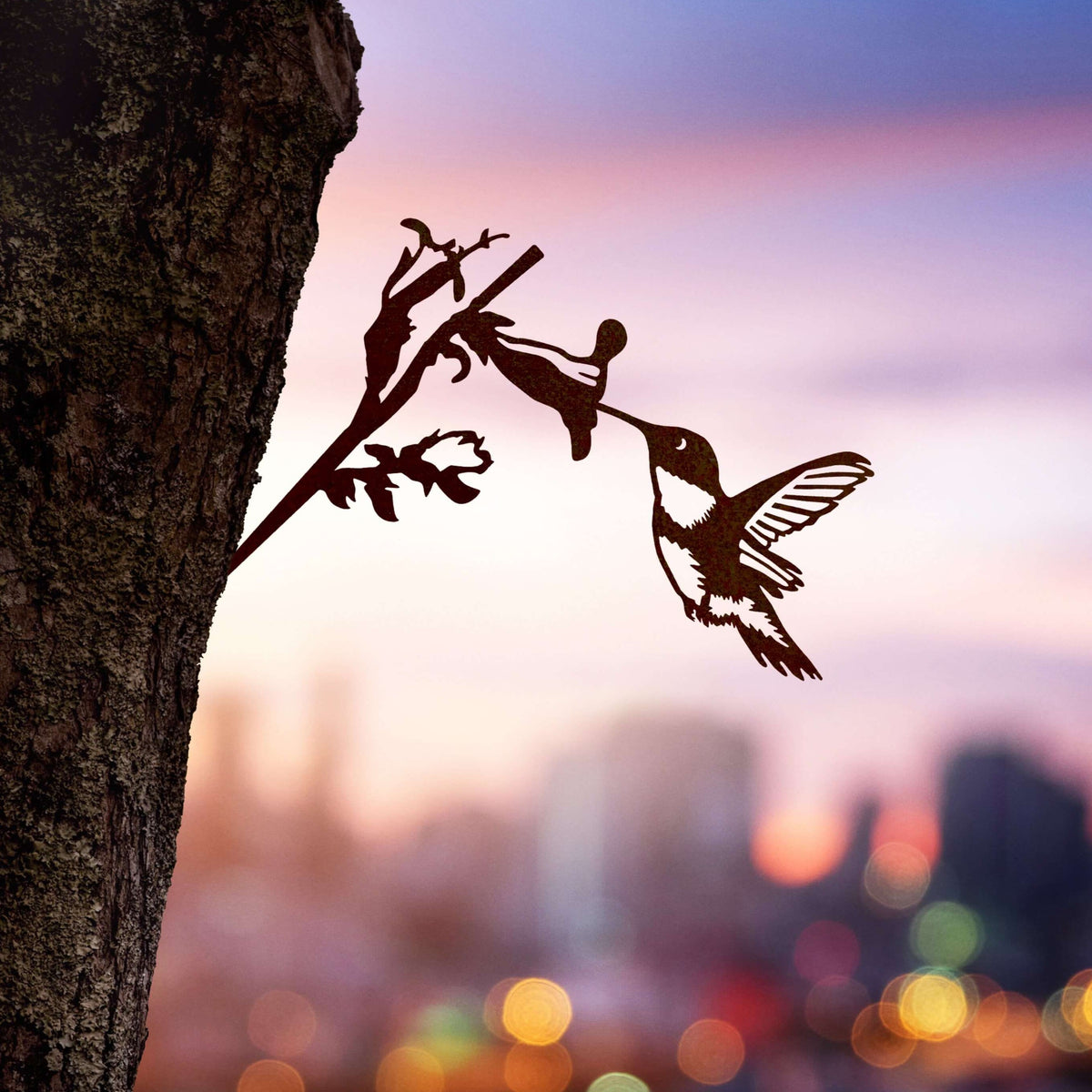 Hummingbird steel silhouette and flowering branch mounted beside a tree at dusk.